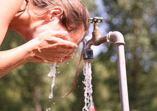 Kvinde vasker sig ansigt ved en udendørs vandhane