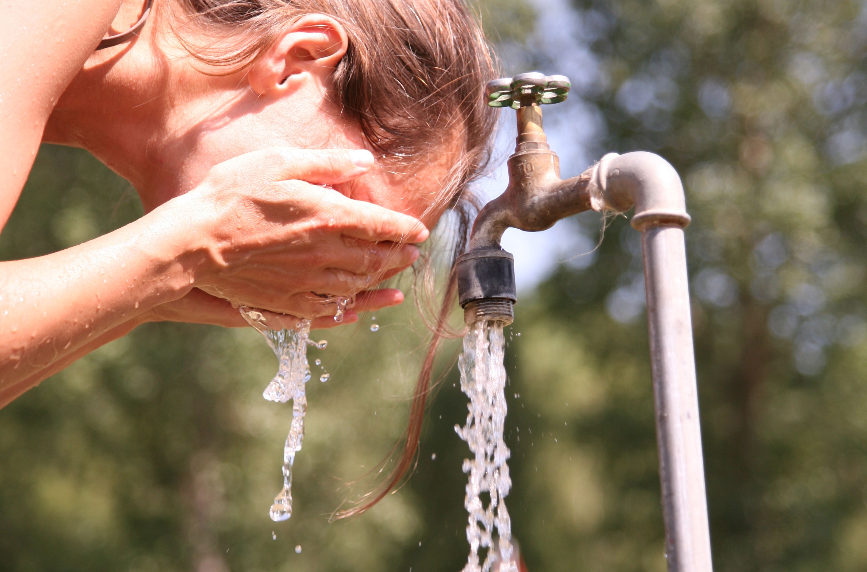 Kvinde vasker sig ansigt ved en udendørs vandhane