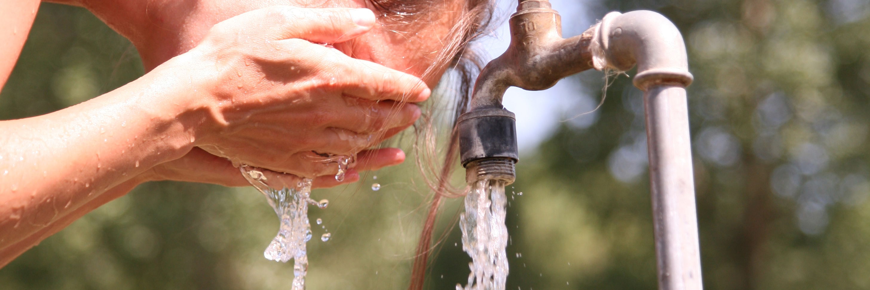 Kvinde vasker sig ansigt ved en udendørs vandhane