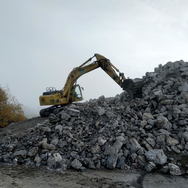 Et bjerg af nedknust beton med en gravemaskine på toppen.
