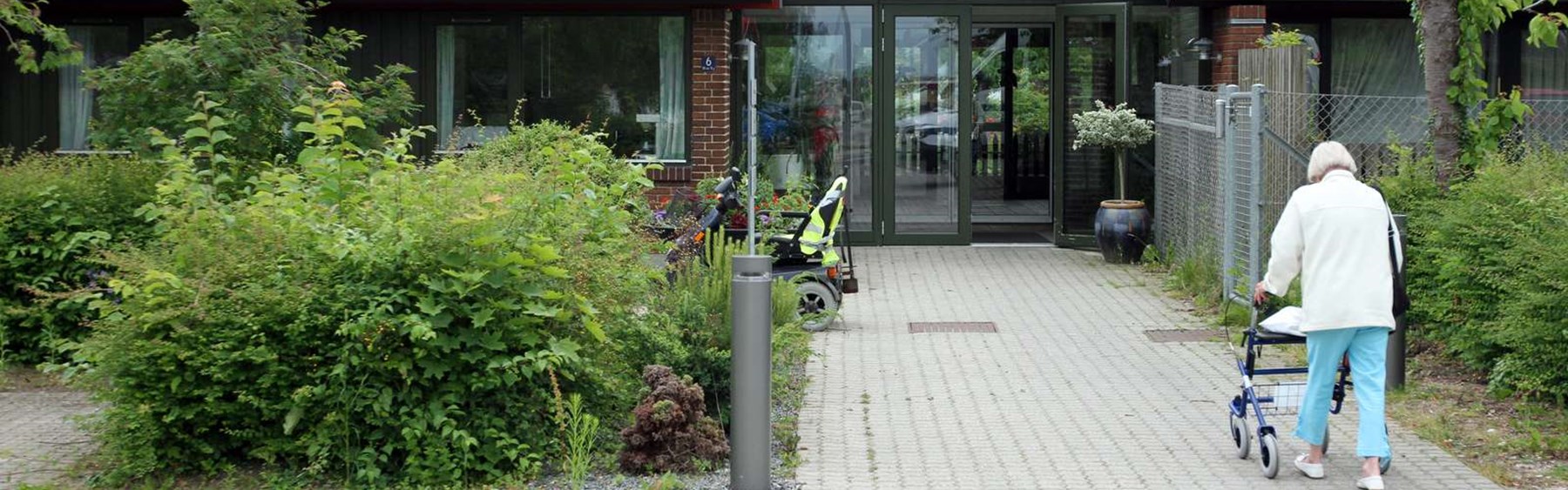 Plejecenter i Roskilde Kommune. En ældre borger med rollator er på vej mod indgangen.