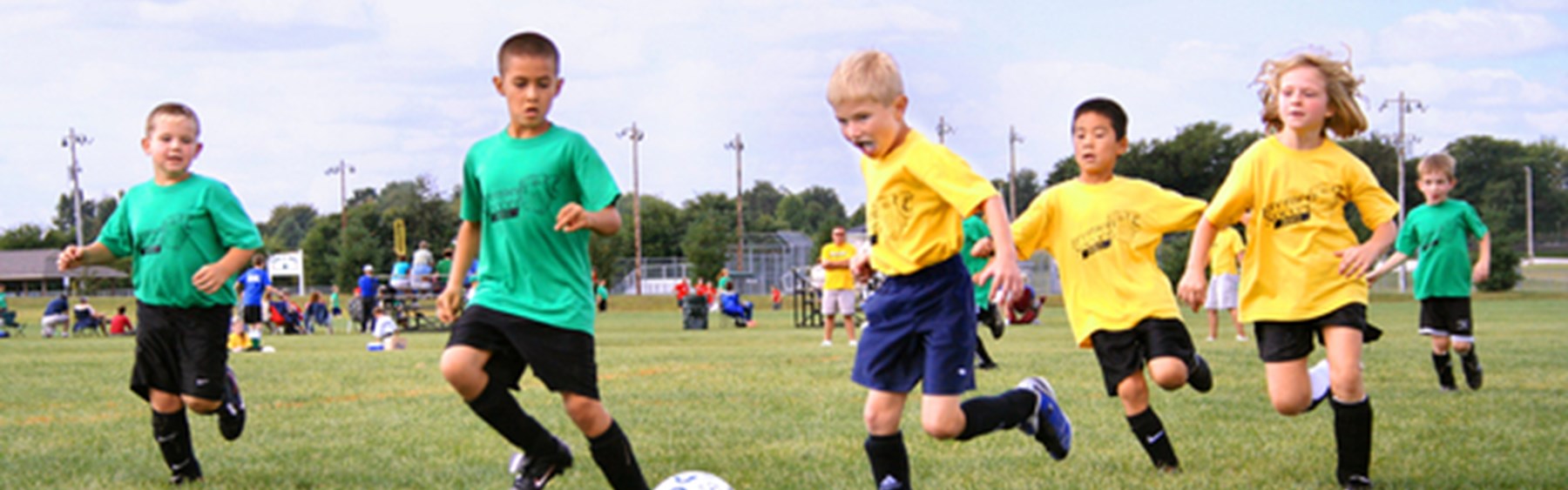 Børn, der spiller fodbold. Nogle af børnene har grønne trøjer på, mens de andres trøjer er gule.