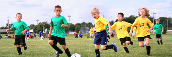 Børn, der spiller fodbold. Nogle af børnene har grønne trøjer på, mens de andres trøjer er gule.
