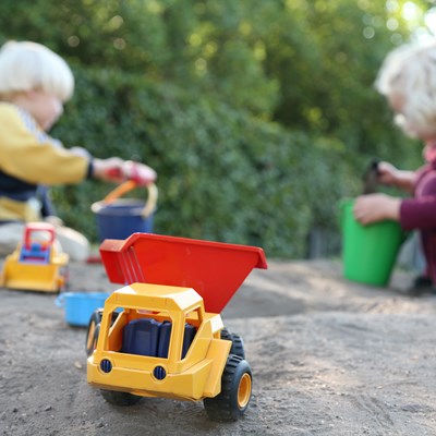 Børn, der leger i en sandkasse. Der er spande og skovle, og der er også små legetøjsbiler.