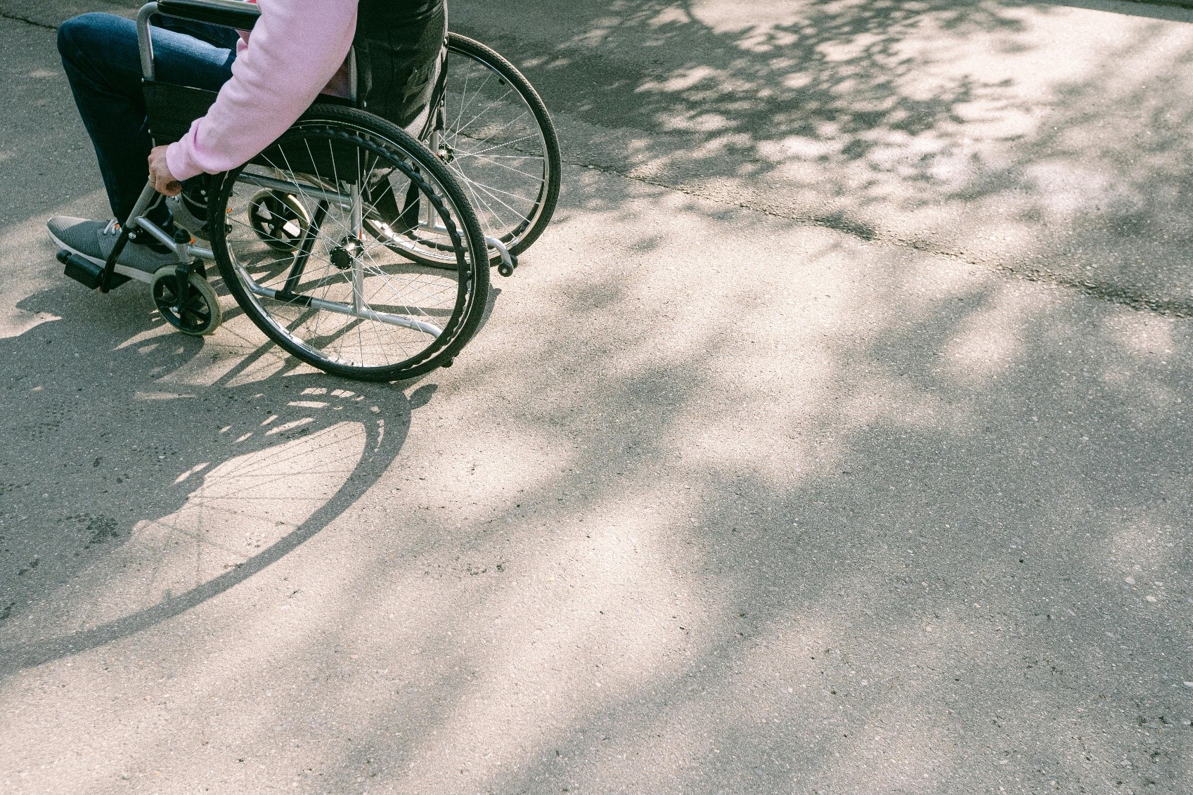 Person med lyserød sweater på sidder i en kørestol. Det er kun kørestolen og personen krop og ben, der er synlige.
