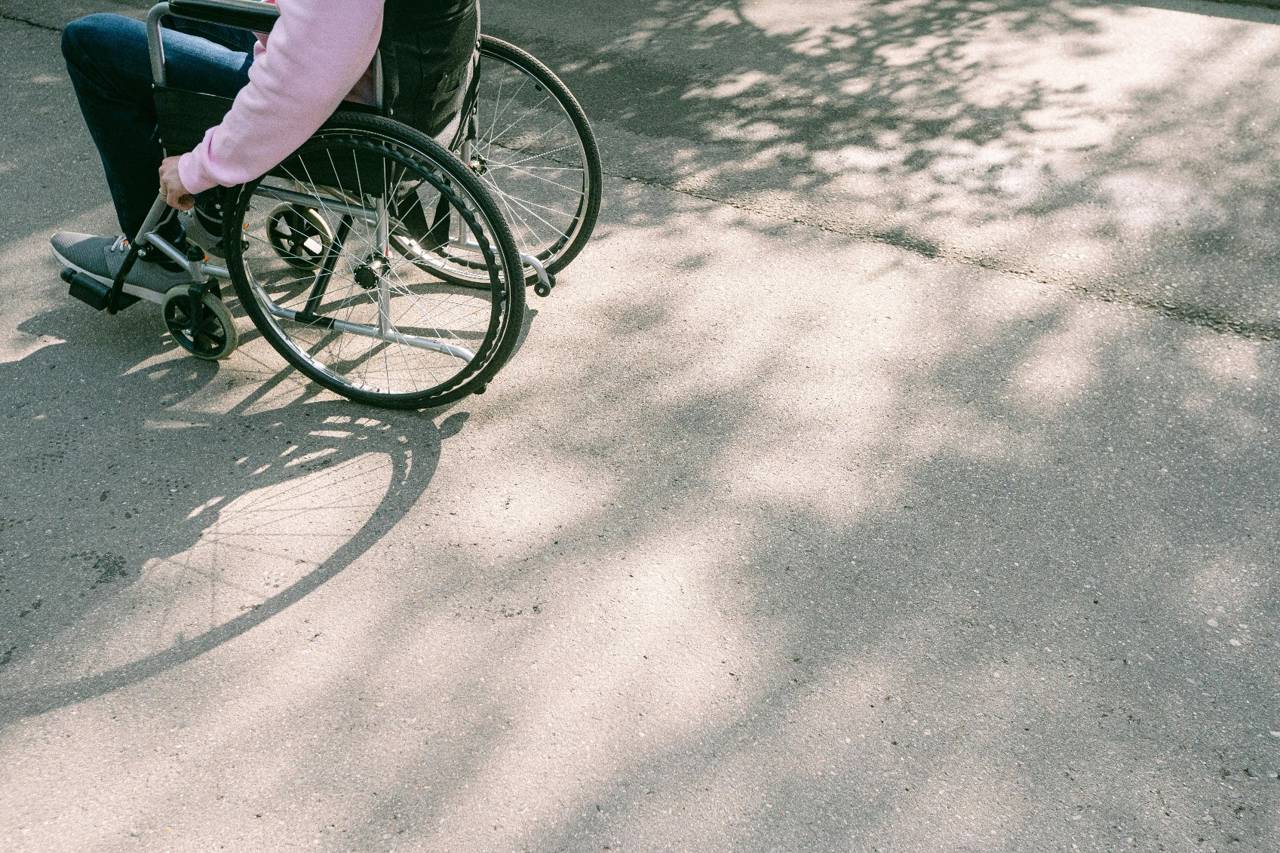 Person med lyserød sweater på sidder i en kørestol. Det er kun kørestolen og personen krop og ben, der er synlige.