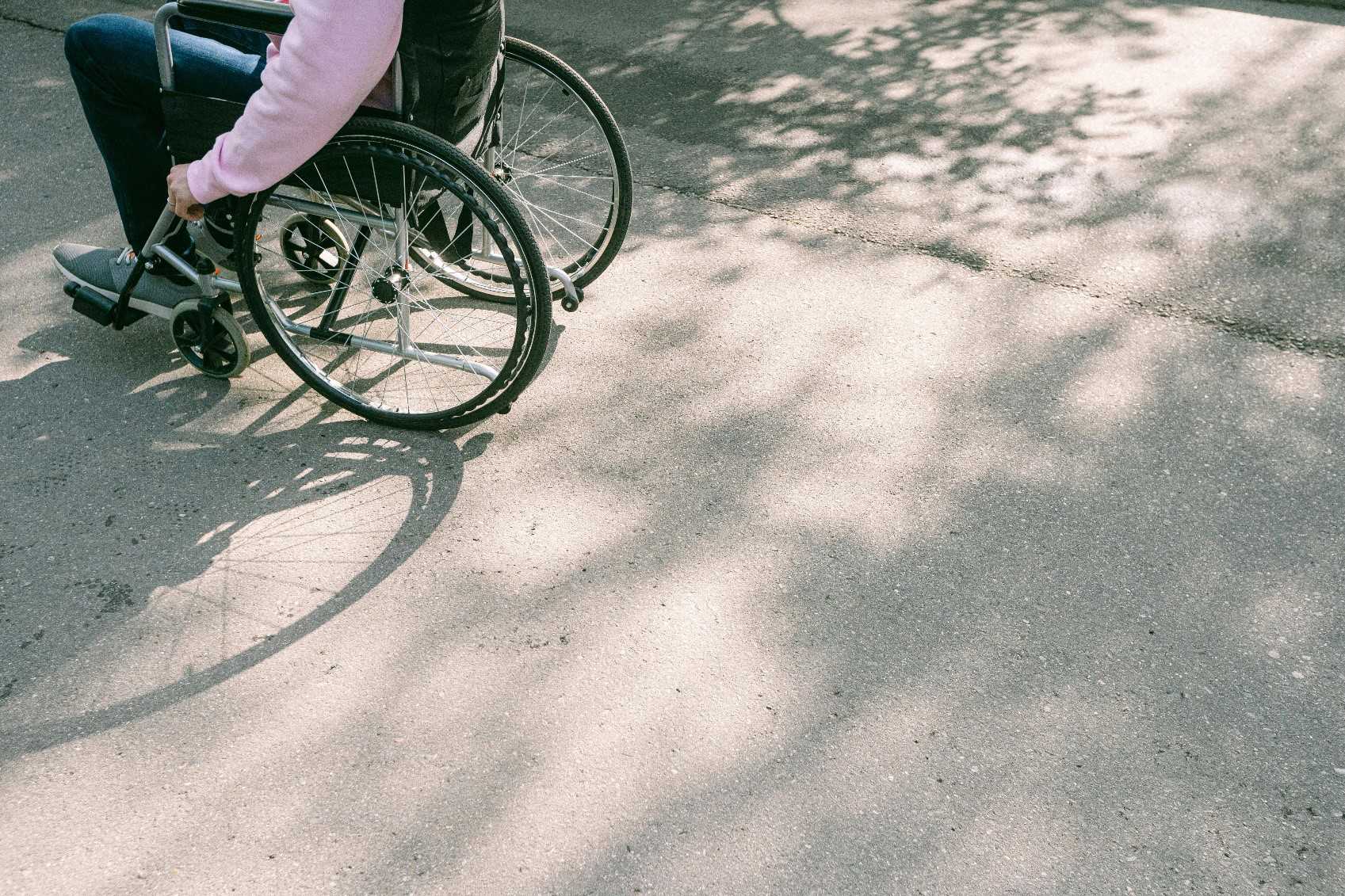 Person med lyserød sweater på sidder i en kørestol. Det er kun kørestolen og personen krop og ben, der er synlige.