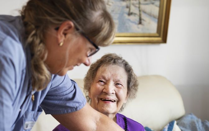 Ældre dame smiler, mens en SOSU-hjælper placerer hendes frokost foran hende.