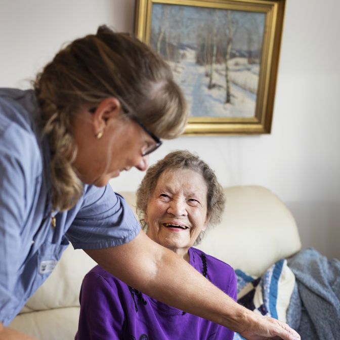 Ældre dame smiler, mens en SOSU-hjælper placerer hendes frokost foran hende.