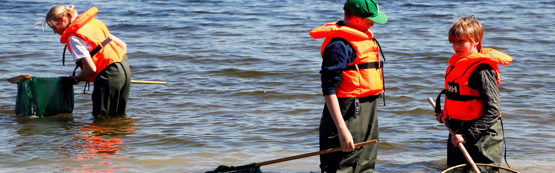 Tre elever med waders fisker med ketsjer i fjorden