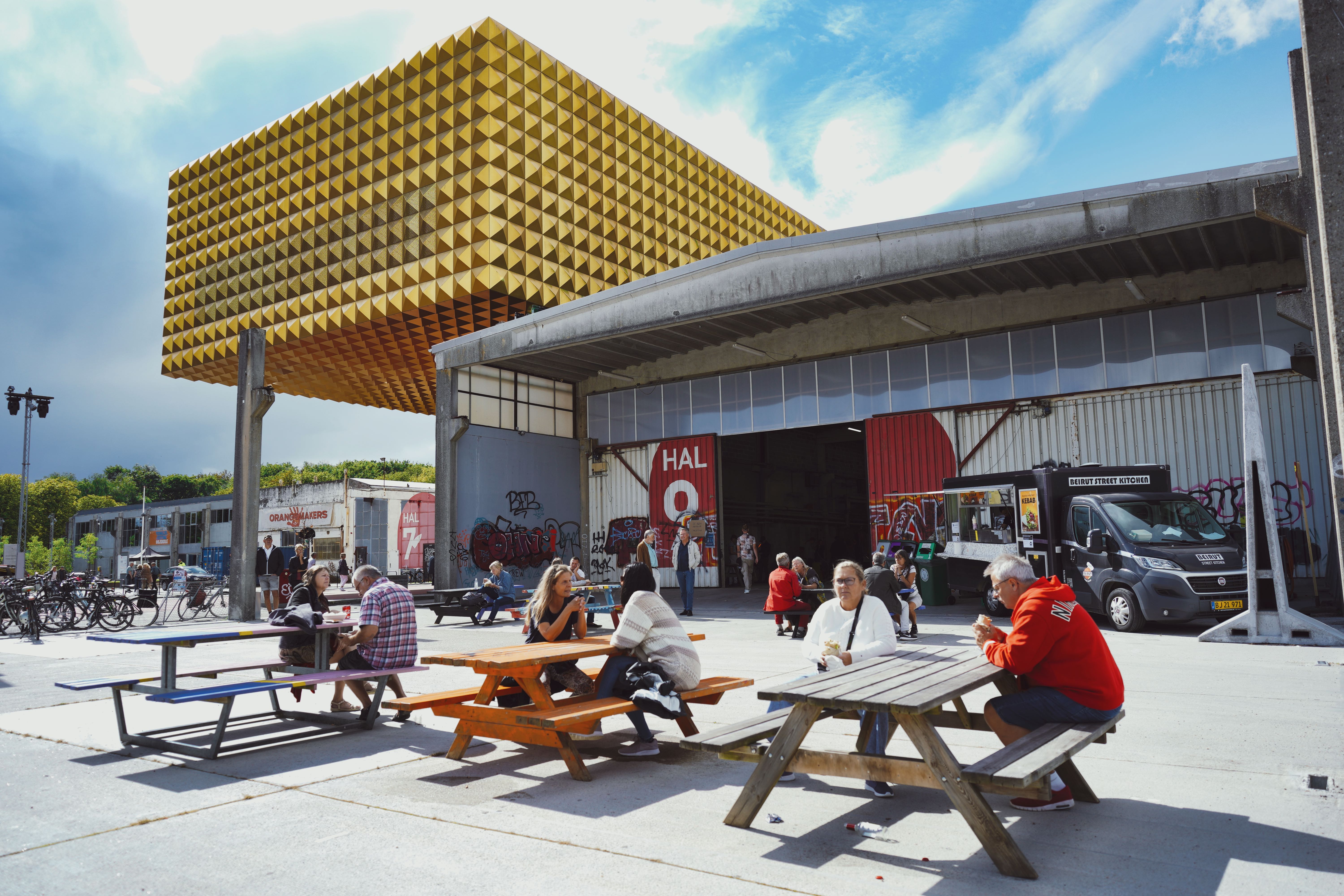 Folk sidder ved bænke på Søjlepladsen foran Hal 9