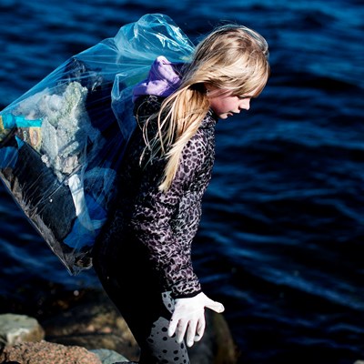 Pige bærer pose med affald ved fjorden
