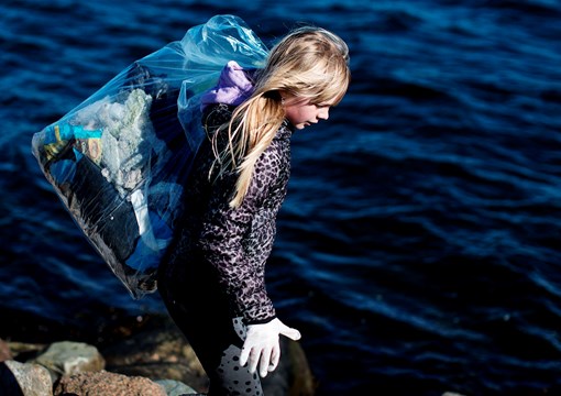 Pige bærer pose med affald ved fjorden