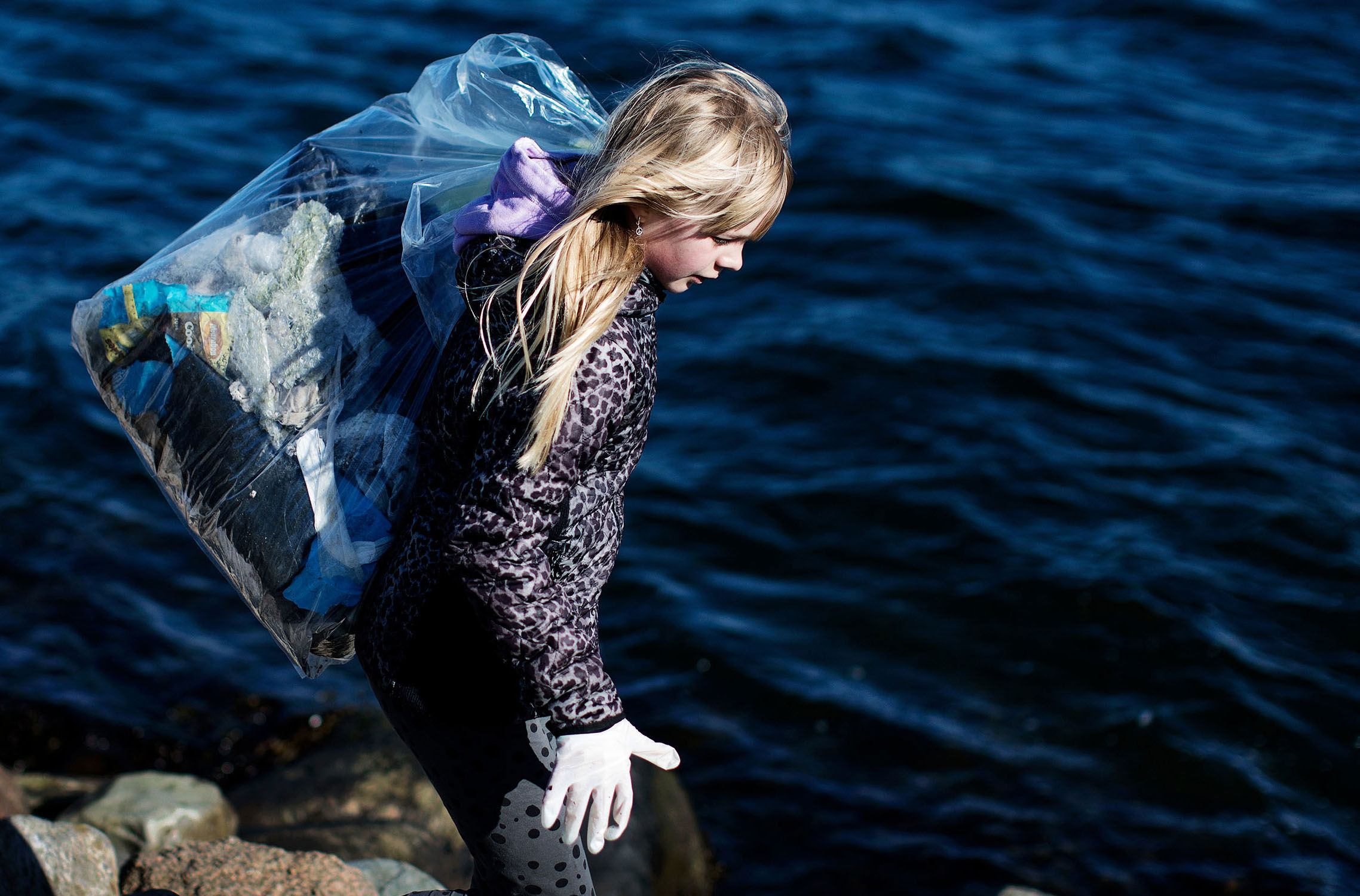 Pige bærer pose med affald ved fjorden