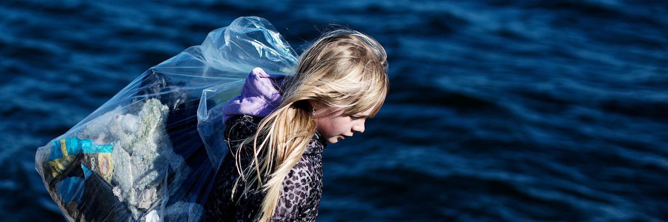 Pige bærer pose med affald ved fjorden