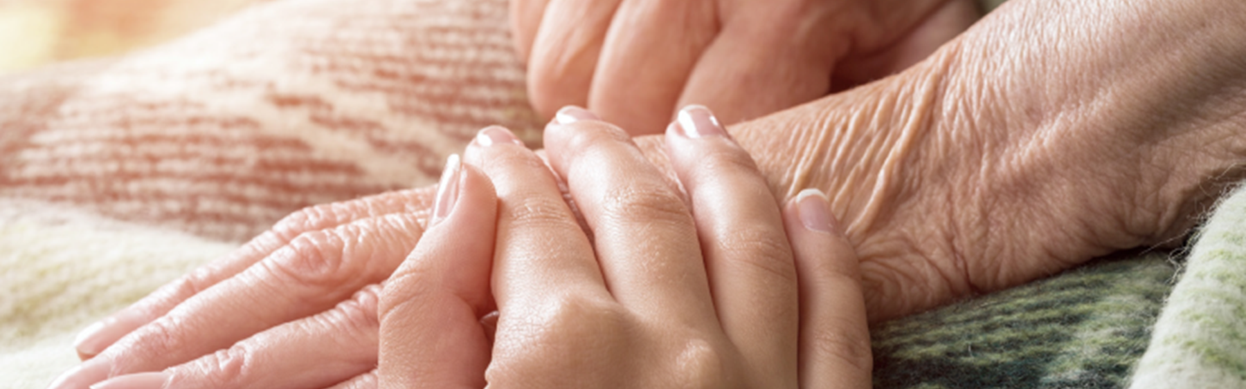 En yngre kvinde holder en ældre borger i hånden. Deres hænder ligger på et tæppe på den ældre persons skød.