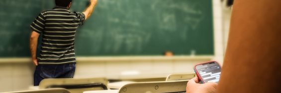 Lærer står foran tavle. han er ved at skrive på den. Der sidder en elev og følger med.