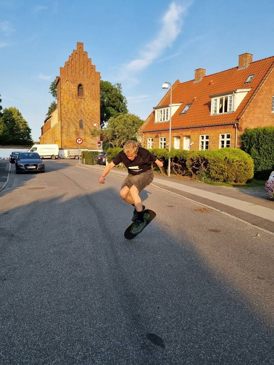 Ung man, der skateboarder ned ad en asfalteret vej. Han er ved at lave et kick-flip.