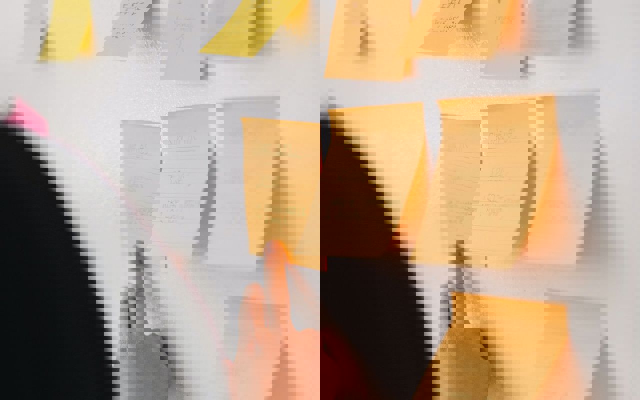 Person, der sætter en note på en væg. Der hænger flere noter på væggen.