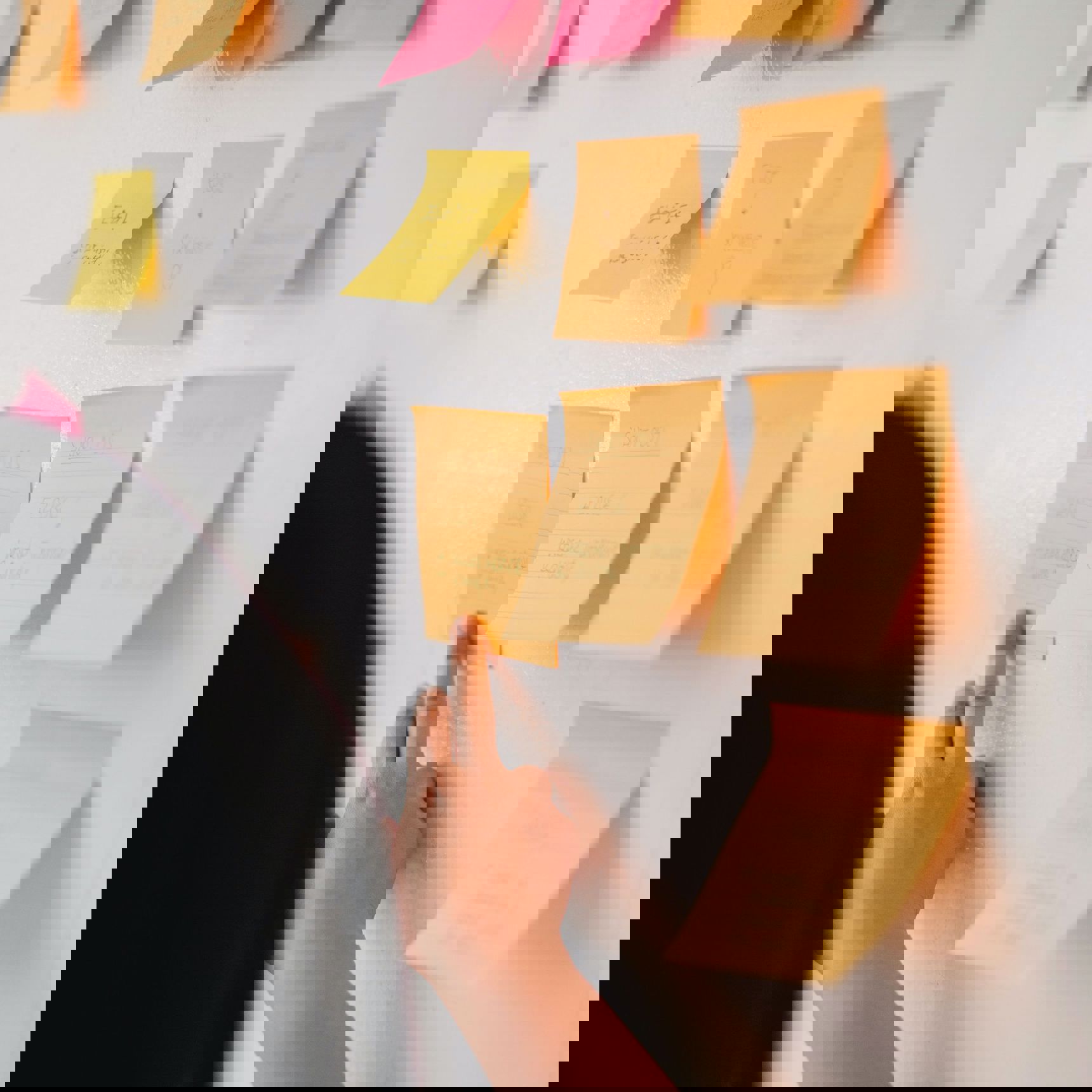 Person, der sætter en note på en væg. Der hænger flere noter på væggen.