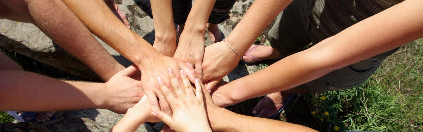 En masse personer står i en cirkel og har deres hænder samlet på midten. Det symboliserer, at de samarbejder og hjælper hinanden.