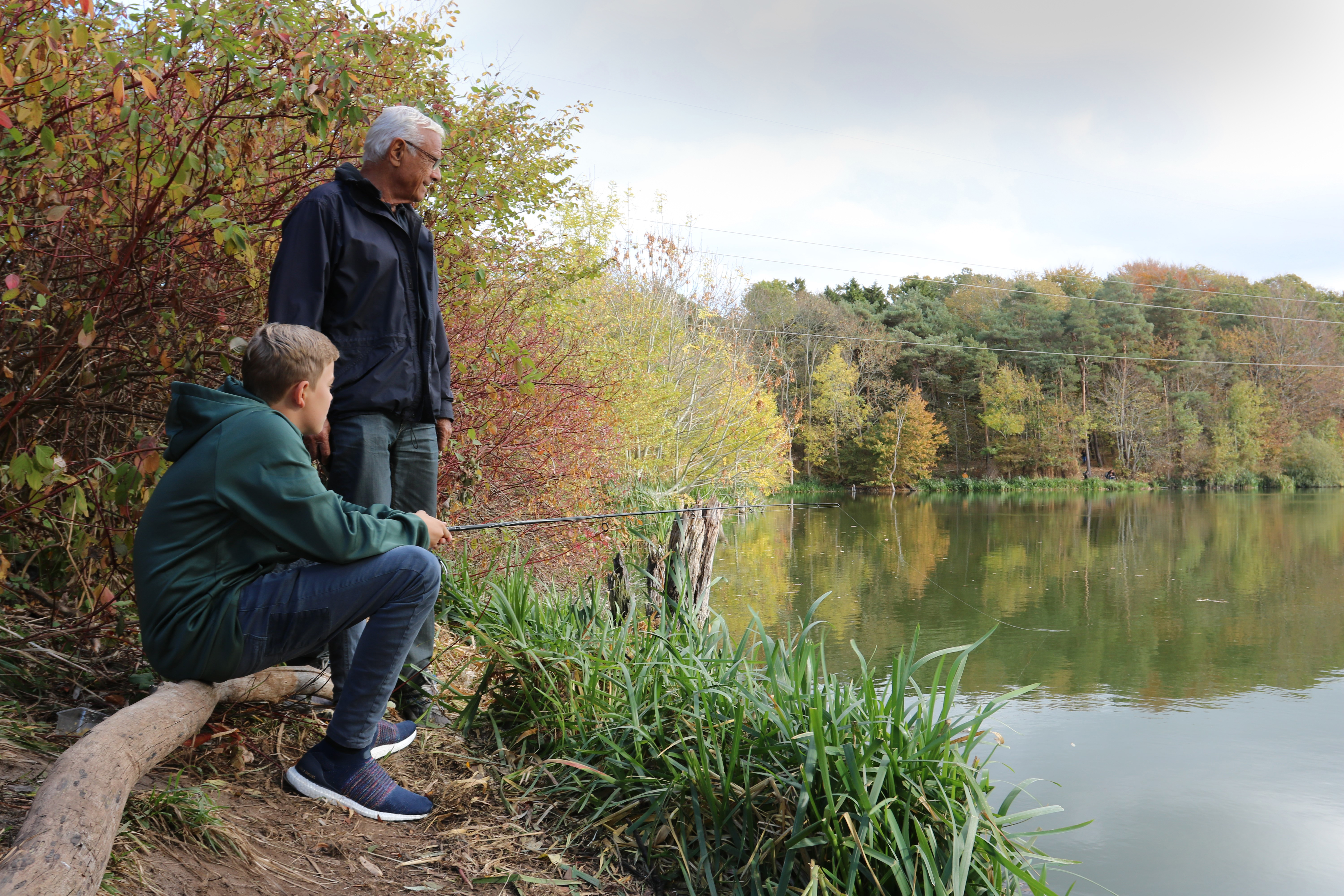 Bedstefar og barnebarn fanger fisk ved sø.